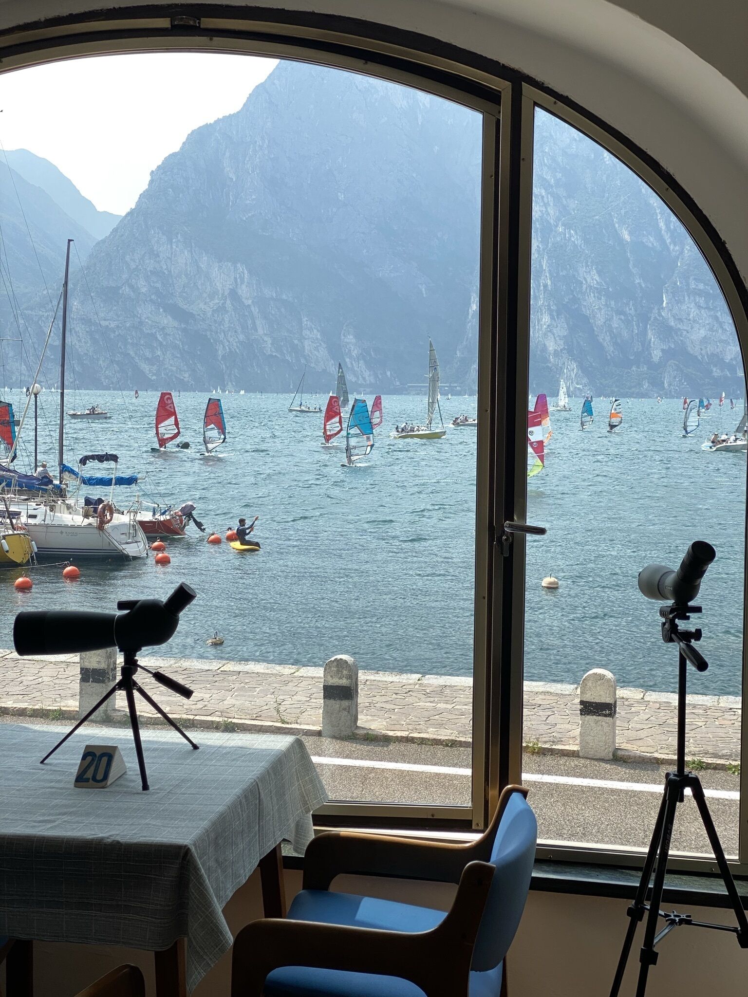 Une pièce dotée d’une grande fenêtre donnant sur une marina où sont amarrés des voiliers, avec une chaîne de montagnes en arrière-plan.