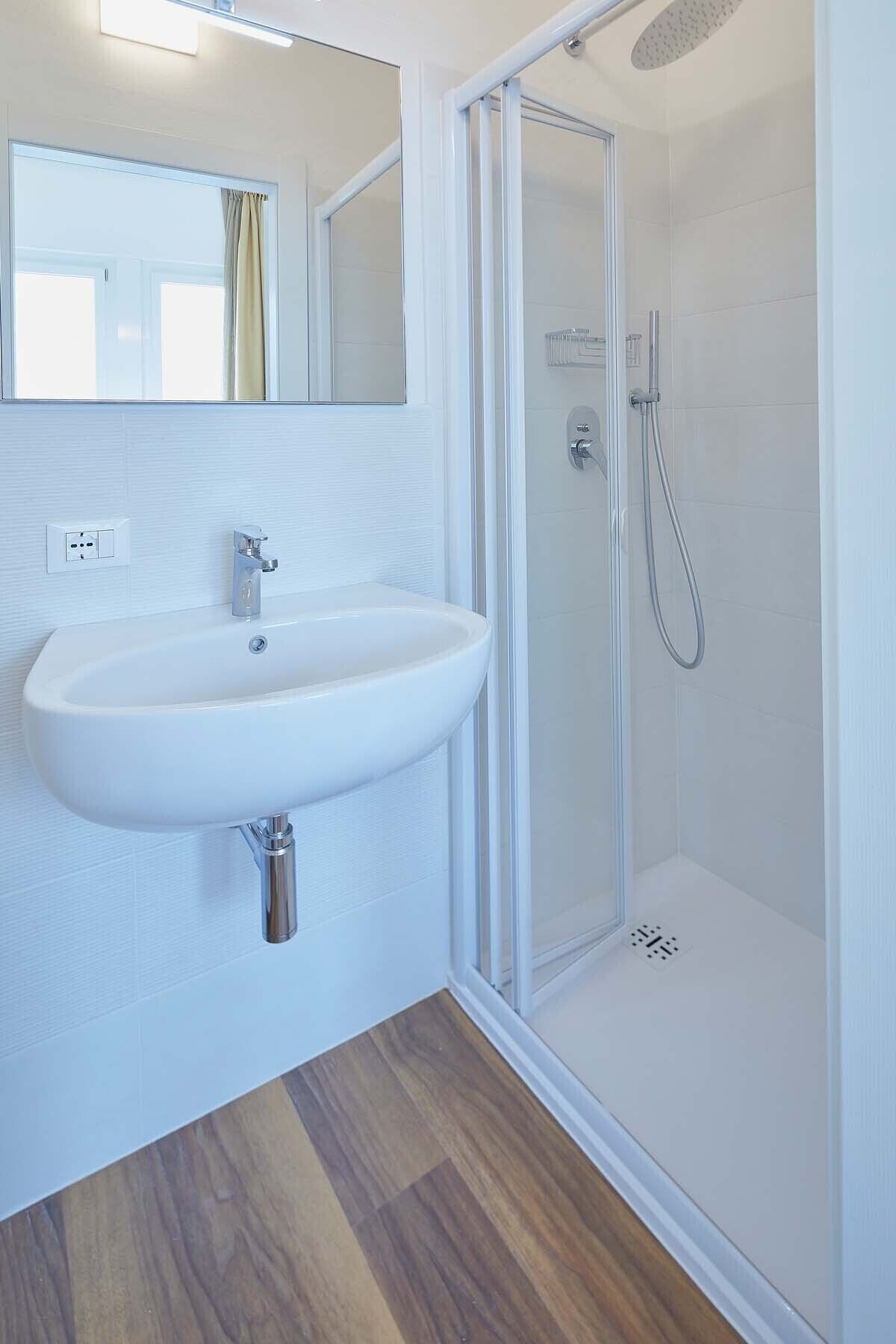A bathroom with a white sink, a glass shower enclosure, and a wooden floor.