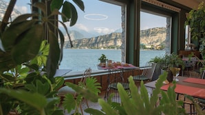 A dining area with a table set for two, overlooking a body of water and mountains. - Hotel Paradiso (Nago-Torbole)