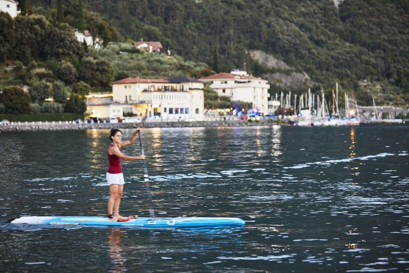A person paddleboarding on a calm body of water with a building and trees in the background.