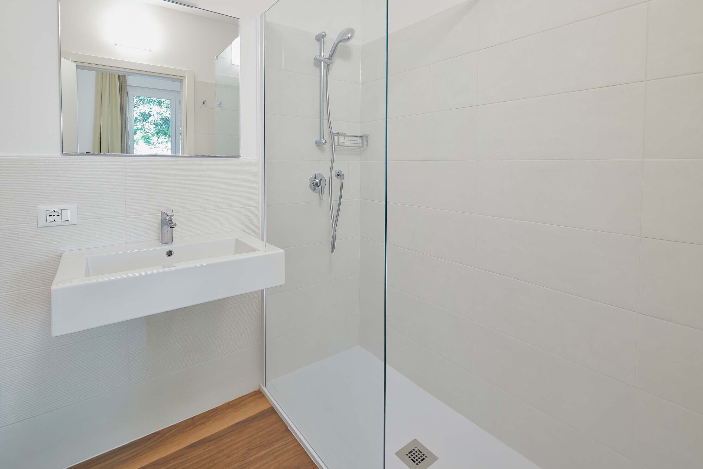 A modern bathroom with a glass shower enclosure, a white sink, and a mirror above the sink.