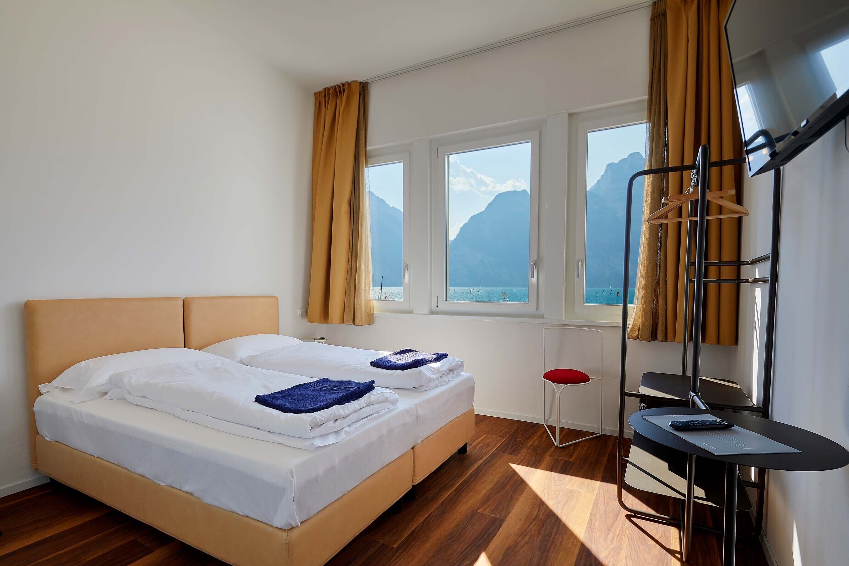A hotel room with a bed, a desk, and a view of mountains through the windows.