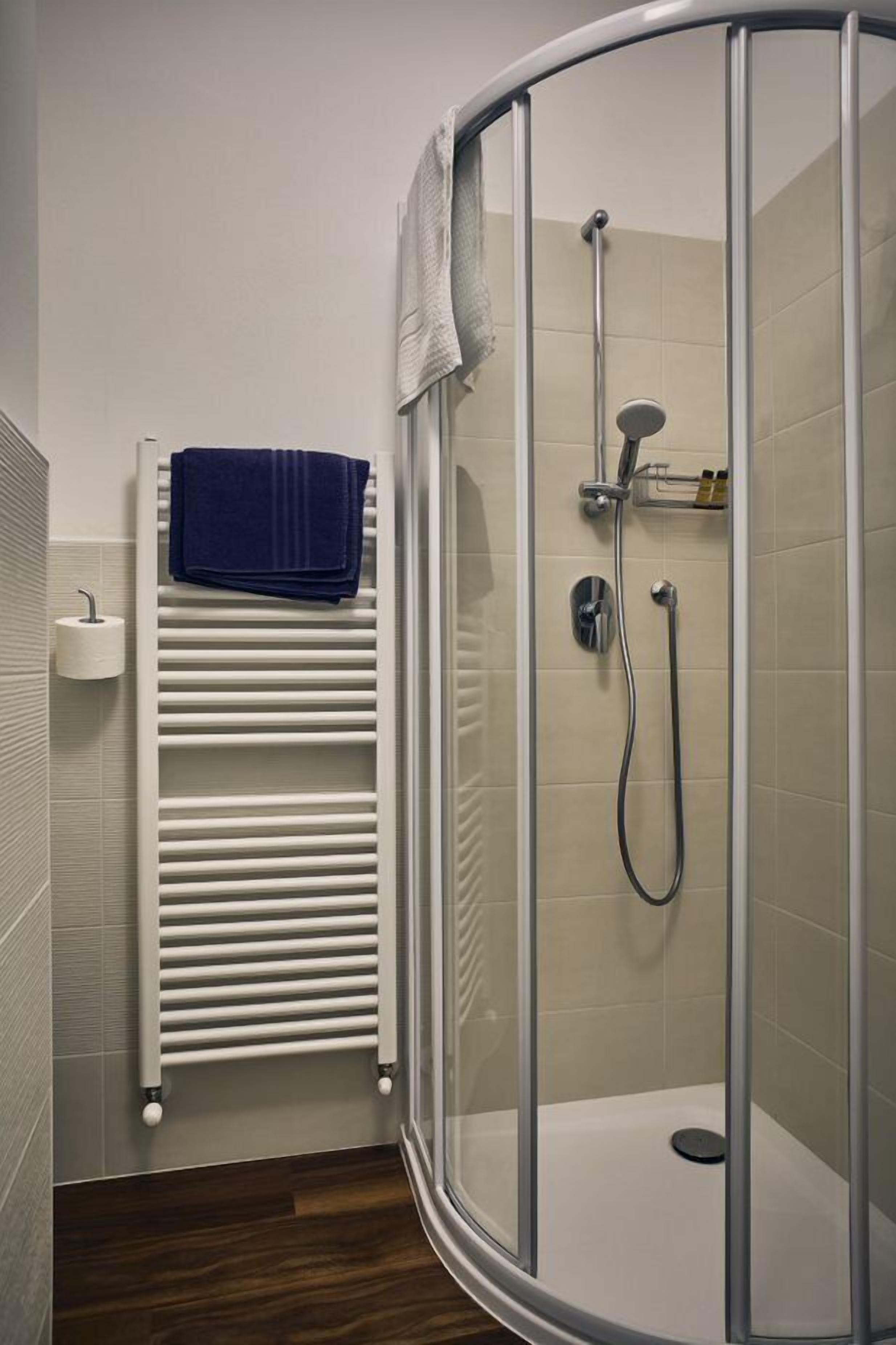 A modern bathroom with a glass-enclosed shower, a white towel rack, and a built-in toilet.