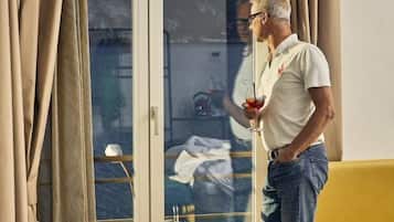 Ein Mann steht an einem Fenster mit Vorhängen und hält ein Getränk.