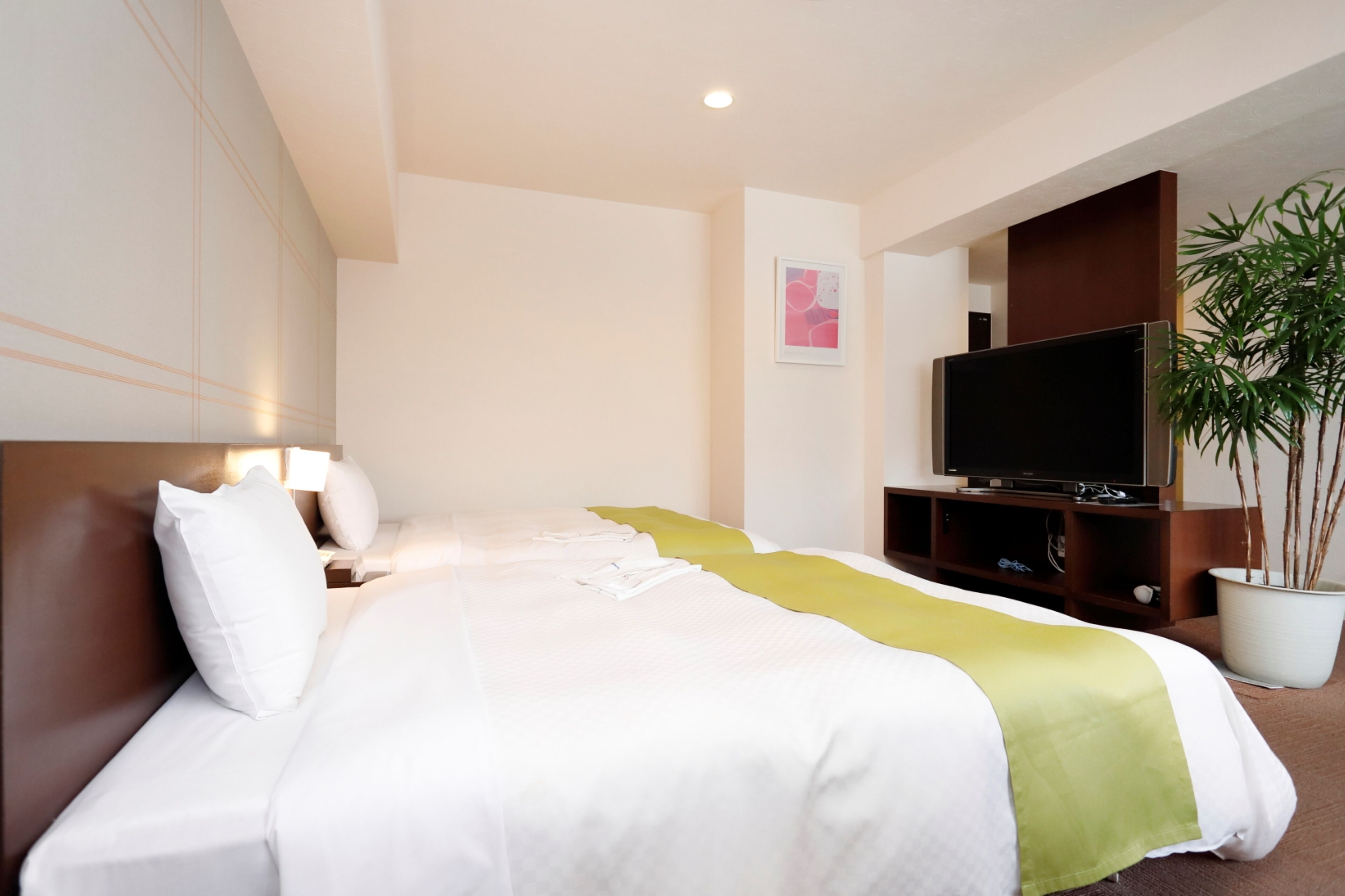 A hotel room with a bed, a television, a plant, and a painting on the wall.
