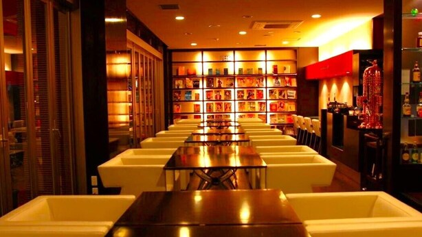 Un vestíbulo de hotel con una larga recepción, asientos blancos acolchados y una estantería llena de libros.