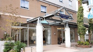 Una entrada moderna a un hotel con fachada de vidrio, zona de acceso cubierta y cartel del Kurume Hotel.