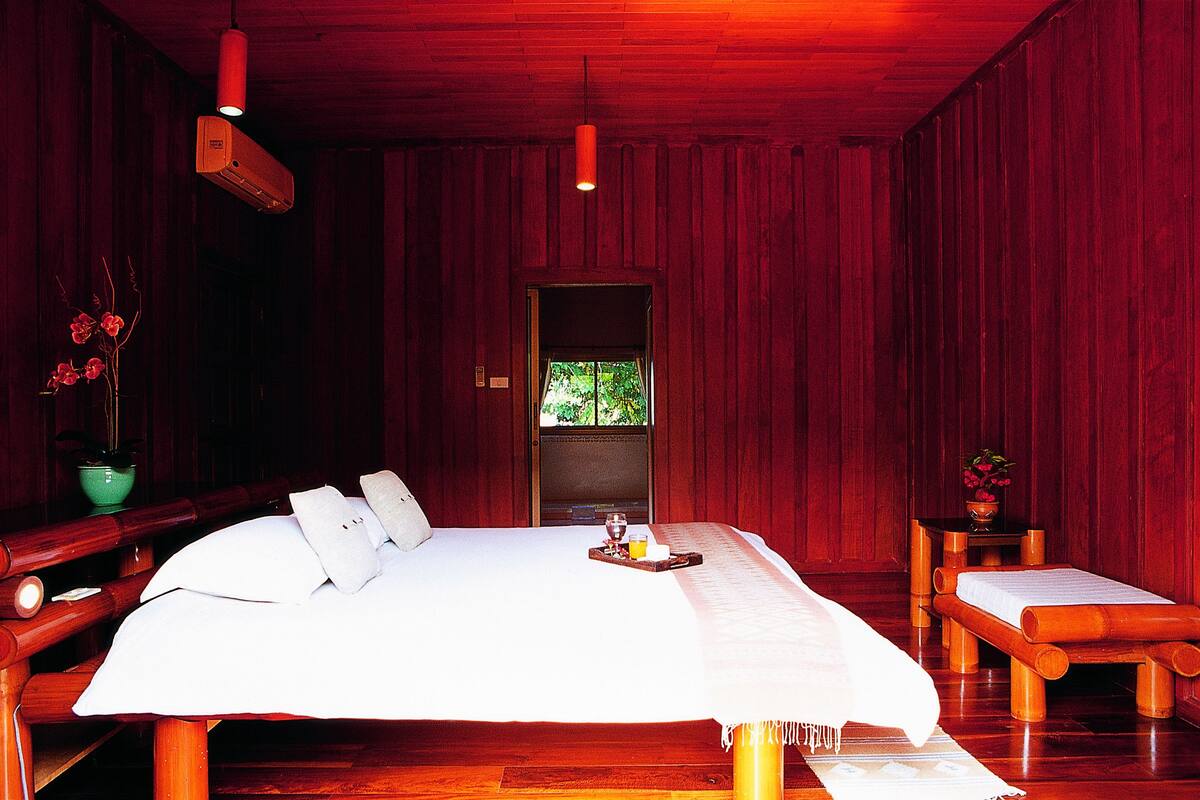 A large bed with a tray of breakfast items, a bedside table with a vase of flowers, and a bench with a towel.