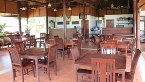 Un comedor amplio con mesas y sillas de madera, suelo de baldosas y techo de paja.