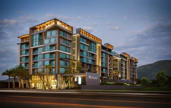 A multi-story hotel with a modern design, featuring a prominent entrance with a sign, multiple balconies, and a view of the surrounding landscape.