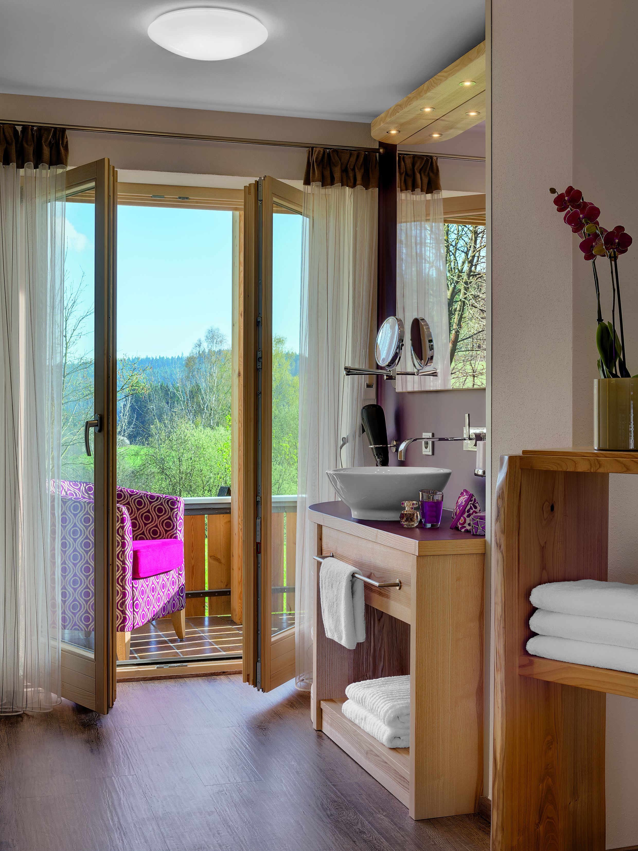 A bathroom with a wooden vanity, a sink, a mirror, and a view of the outdoors.