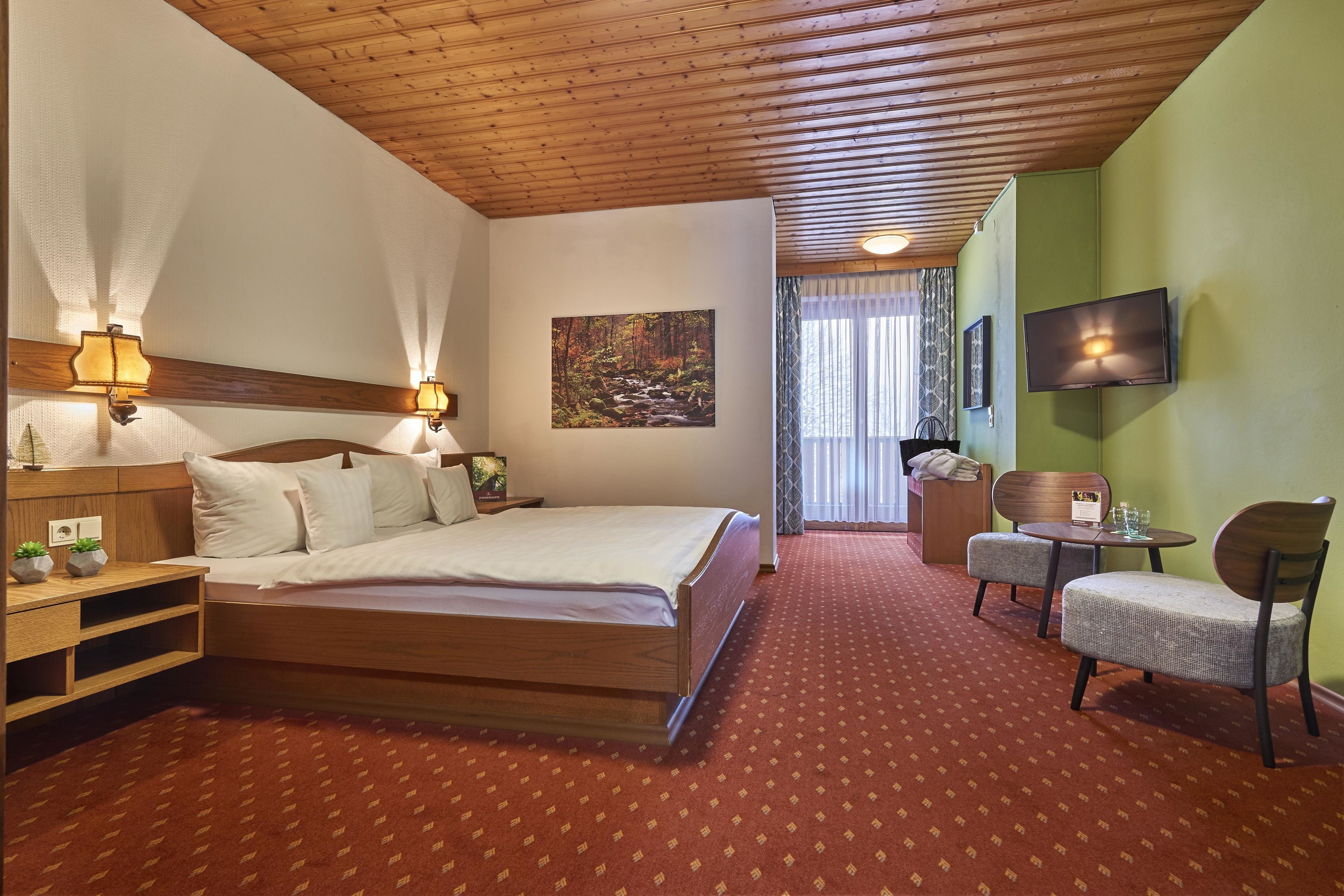 A hotel room with a wooden ceiling, a large bed, a TV, a small table with chairs, and a painting on the wall.
