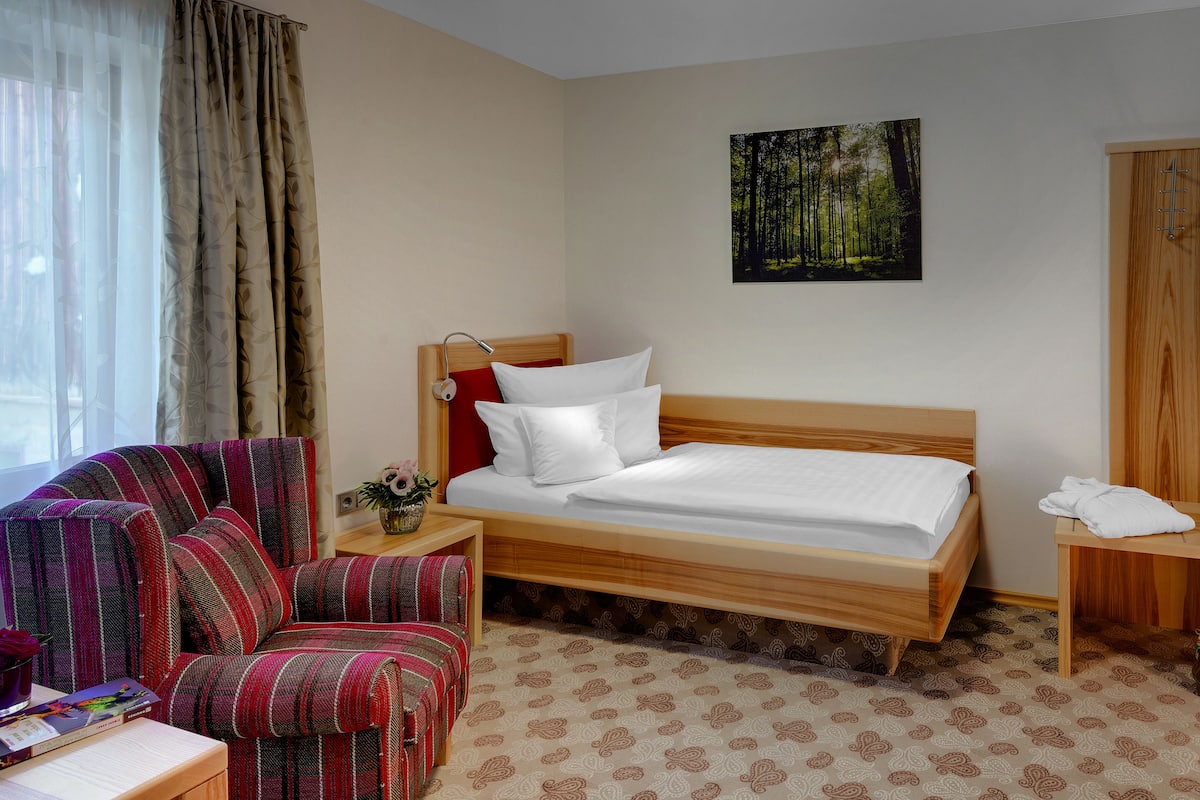 Een hotelkamer met een bed, een televisie, een houten garderobe, een stoel en een kleine tafel met een bloemenvaas.