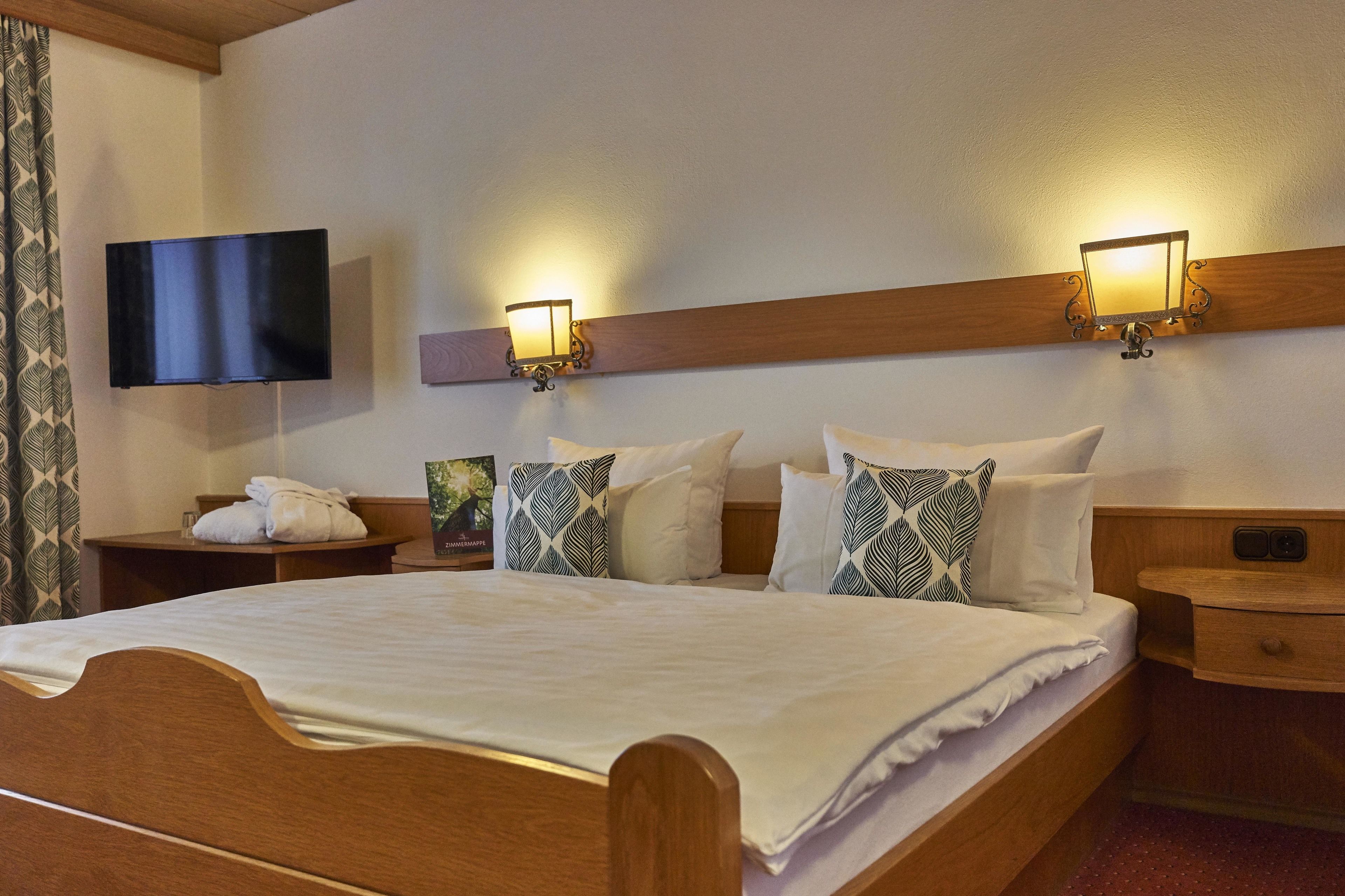 A hotel room with a wooden bed, two bedside tables, a flat-screen TV, and wall-mounted sconces.