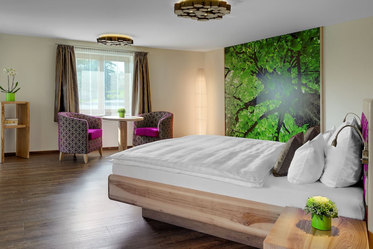 Een hotelkamer met een bed, een stoel, een tafel, een televisie en een groot raam met gordijnen.