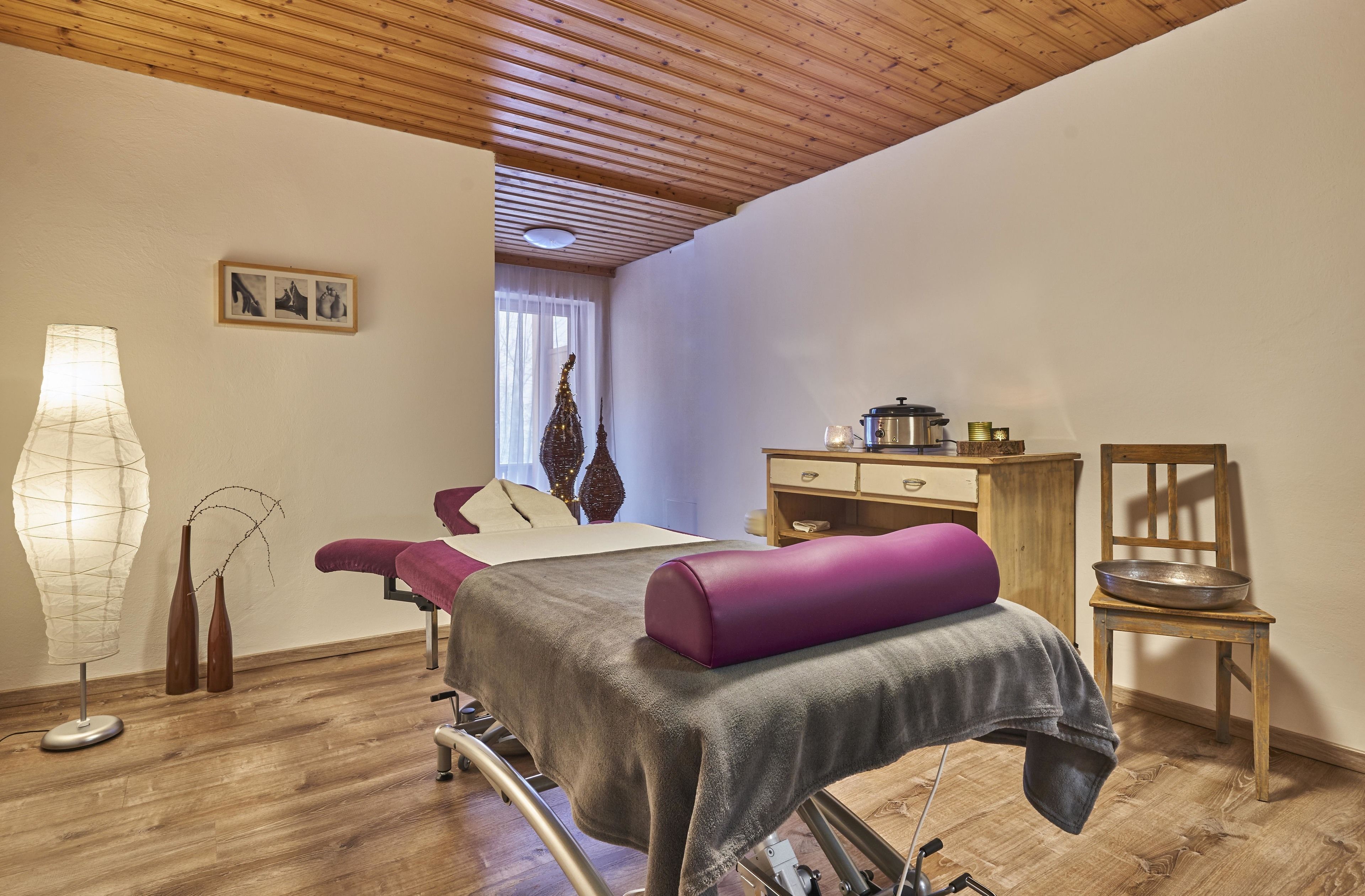 Una habitación con una cama, una mesa de masajes, un armario de madera, una silla y una lámpara.