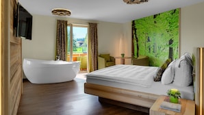 Una habitación de hotel moderna con una cama grande, un baño separado con bañera y un balcón con mobiliario exterior.