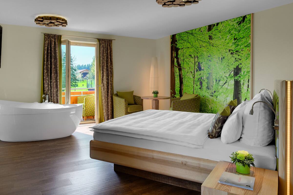 Een moderne hotelkamer met een groot bed, een aparte badkamer met bad en een balkon met zitgelegenheid.