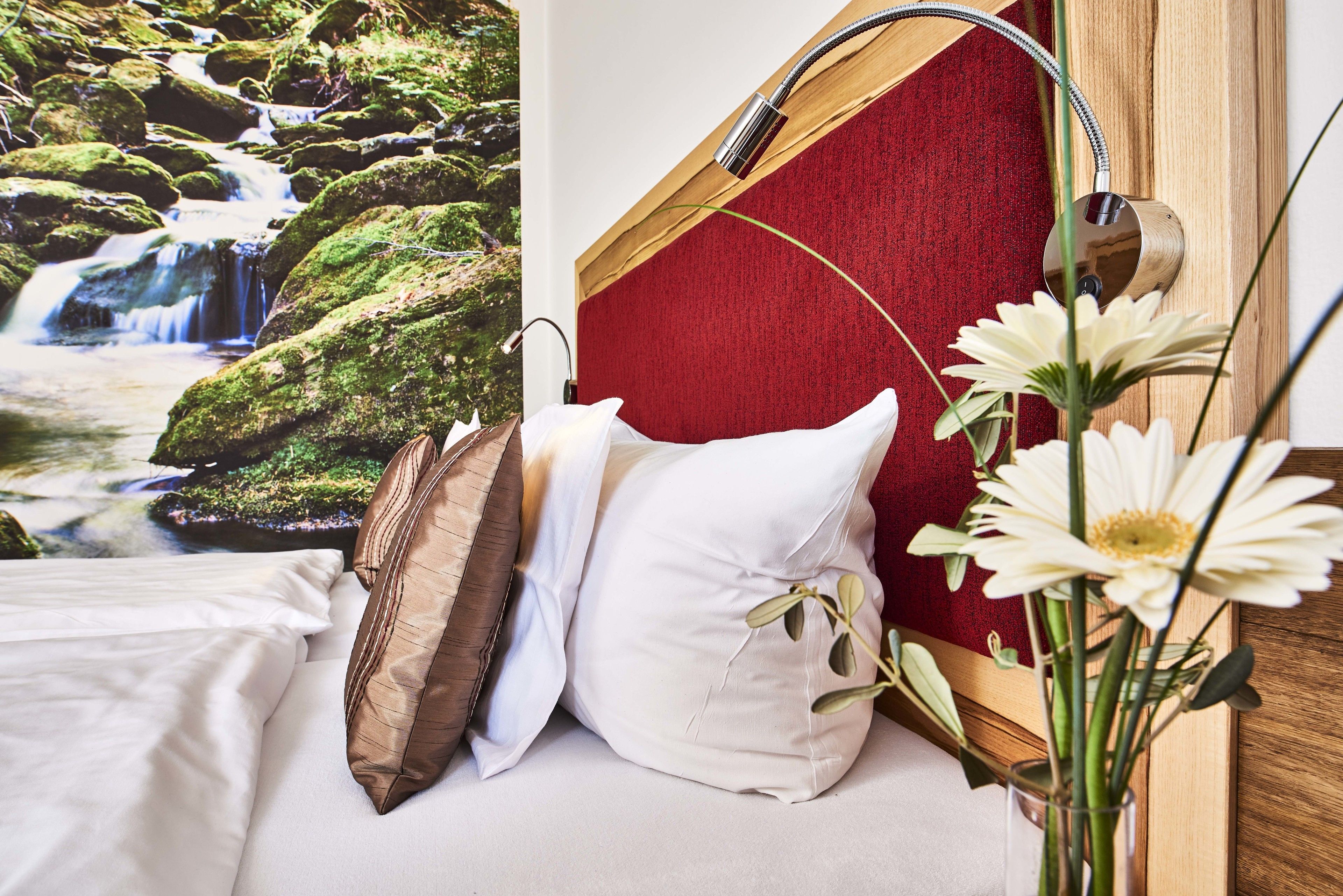 A bed with white and brown pillows, a red headboard, and a wall-mounted shower head.
