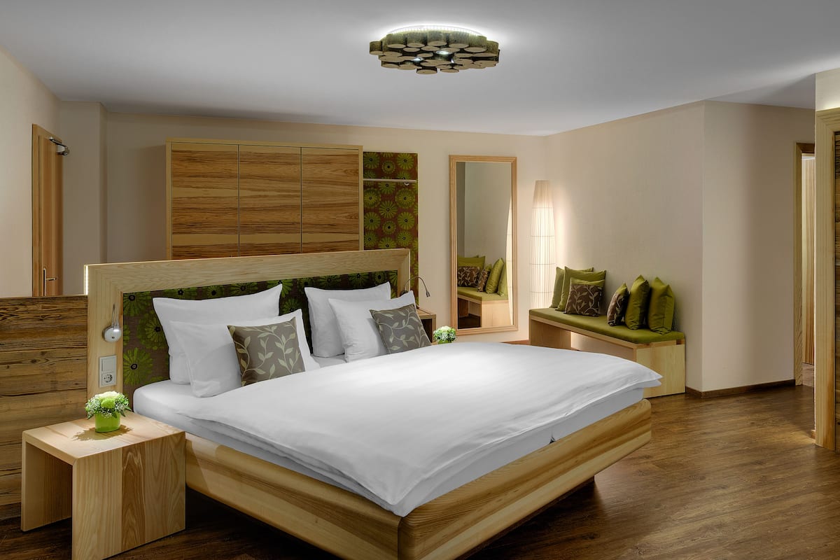 Een moderne slaapkamer met een houten bed, een nachtkastje, een spiegel en een aan de muur bevestigde televisie.