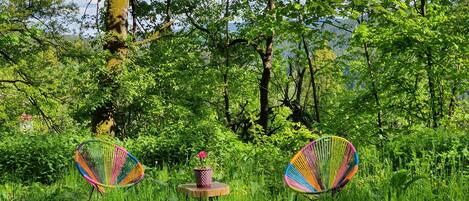 Un sillón hamaca en un bosque verde y frondoso con una pequeña mesa de madera y una planta en maceta.