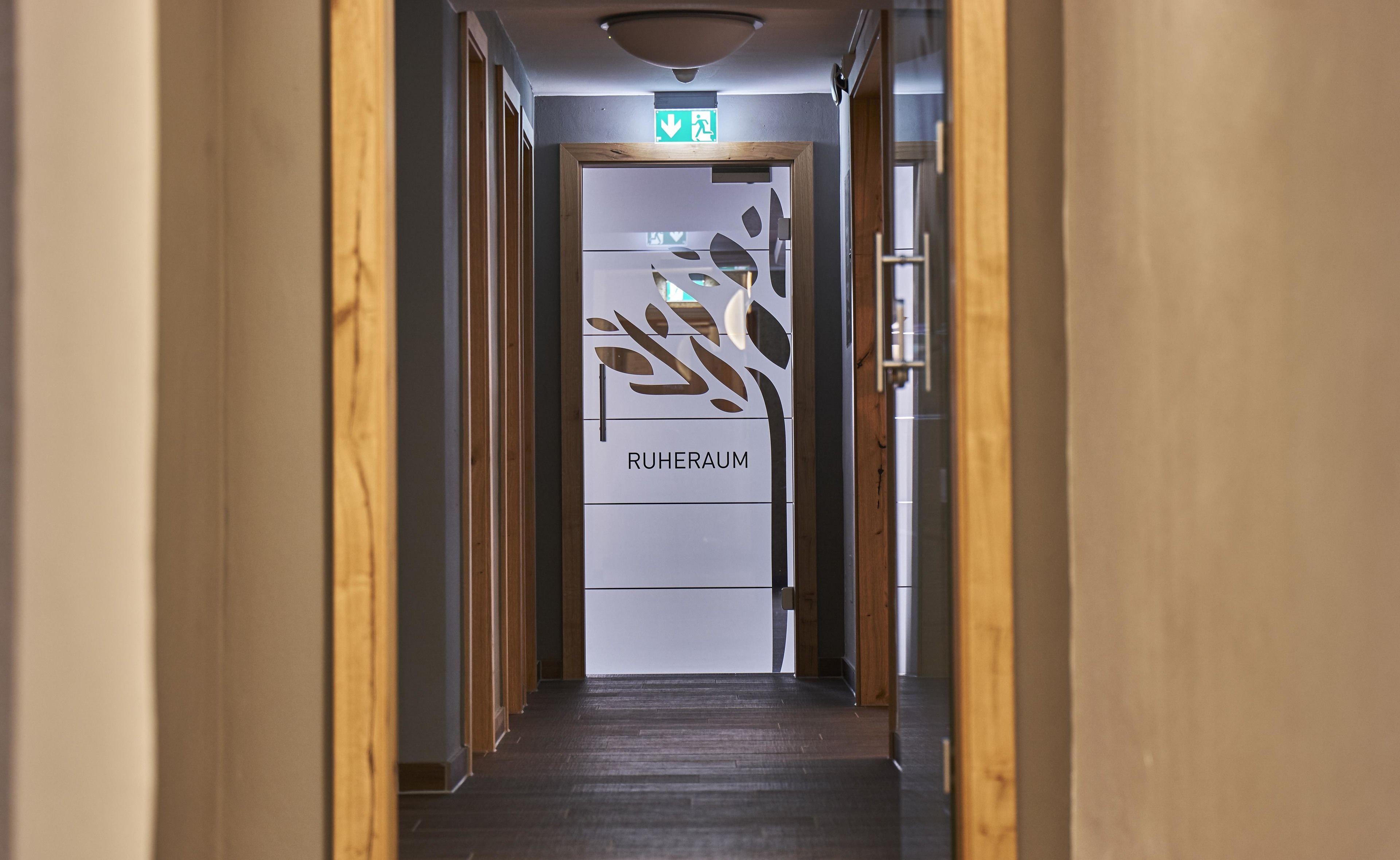Un couloir avec une porte en bois portant l’inscription « RUHERAUM » et un panneau indiquant la sortie de secours au-dessus.