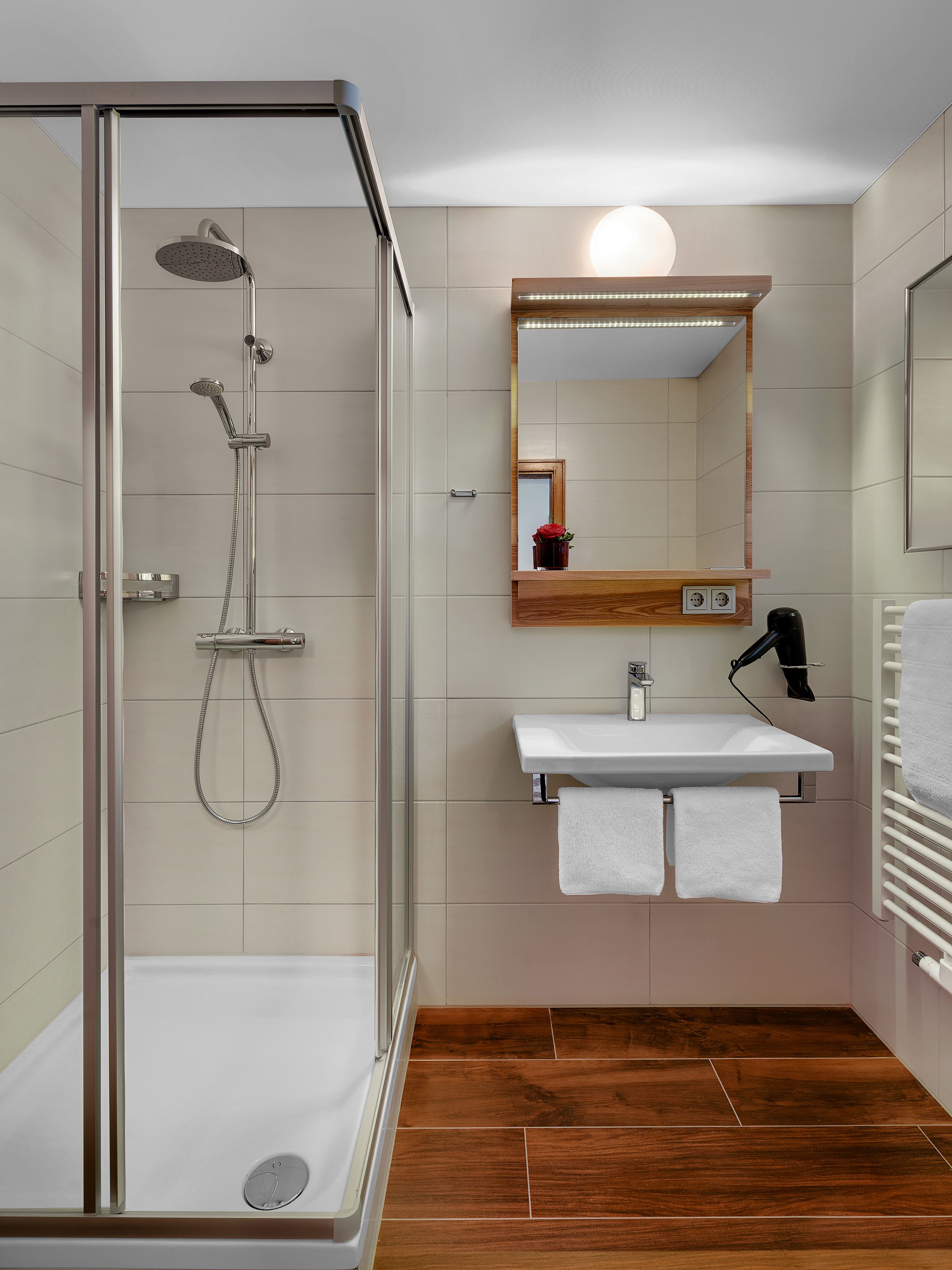 Ein modernes Badezimmer mit einer begehbaren Glasdusche, einem Waschtisch mit Spiegel und einem Handtuchhalter.