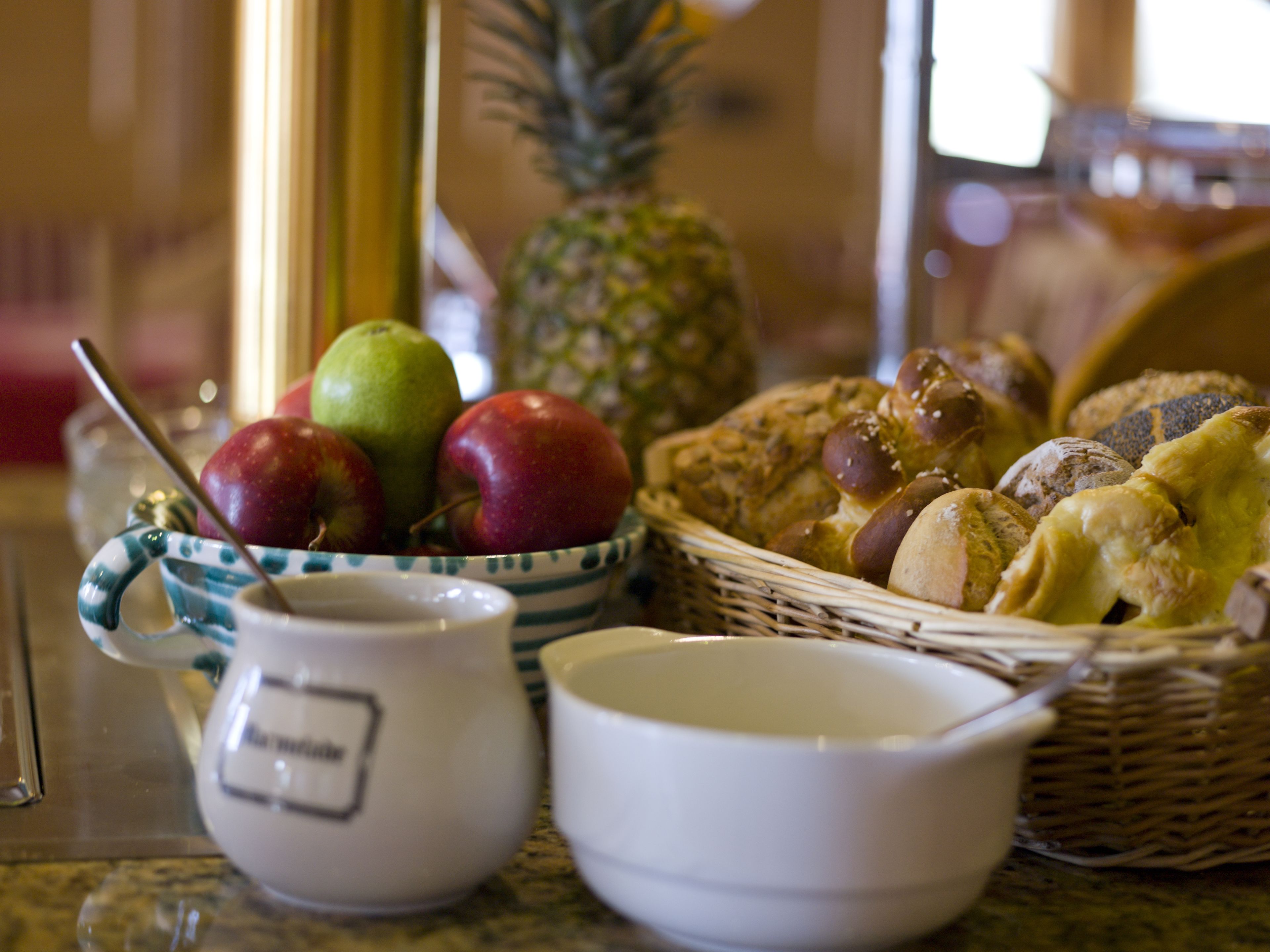 A breakfast table with a bowl of fruit, a basket of bread, and a coffee cup.