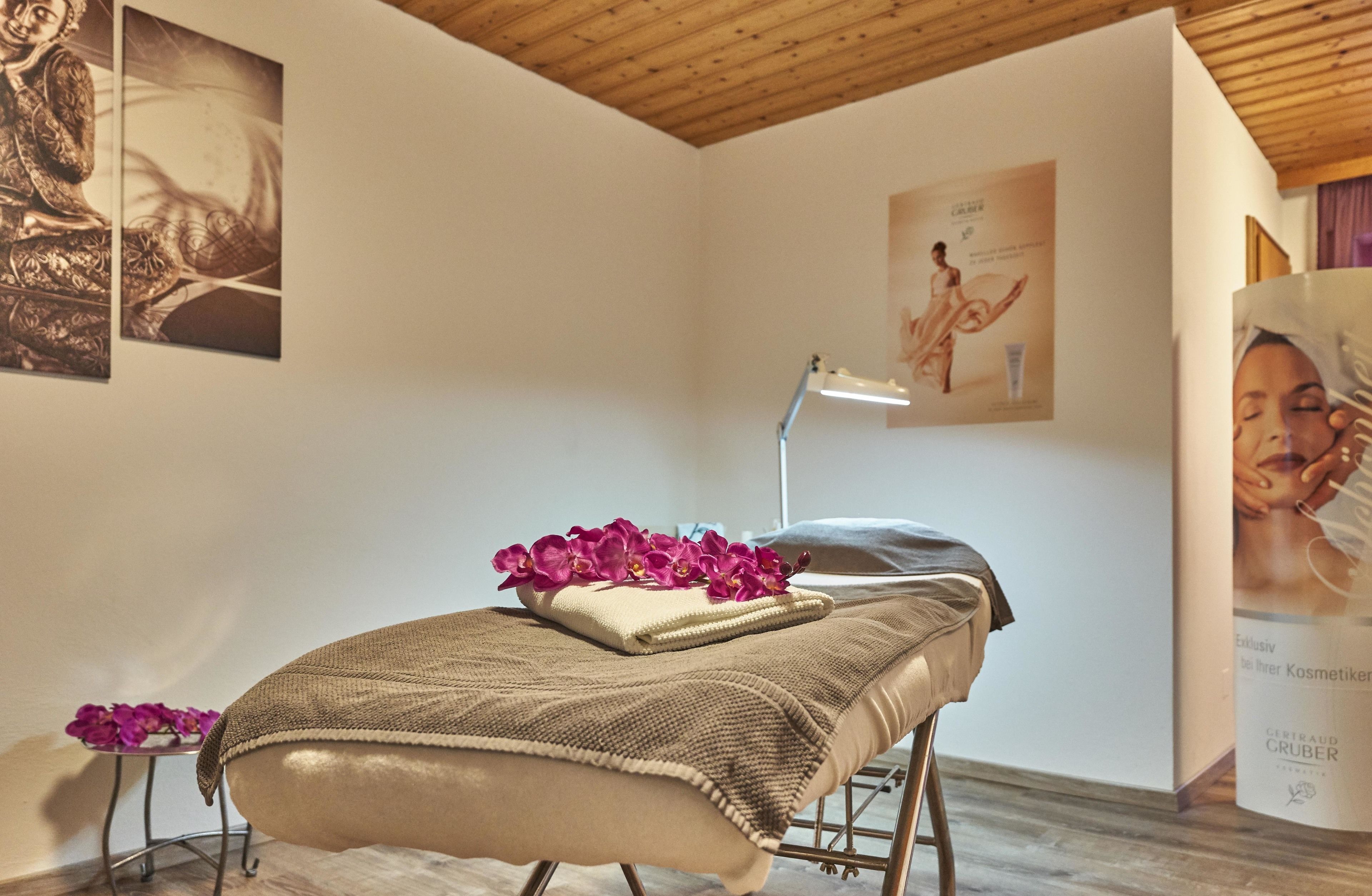 A room with a massage table, a small table with flowers, and a poster on the wall.