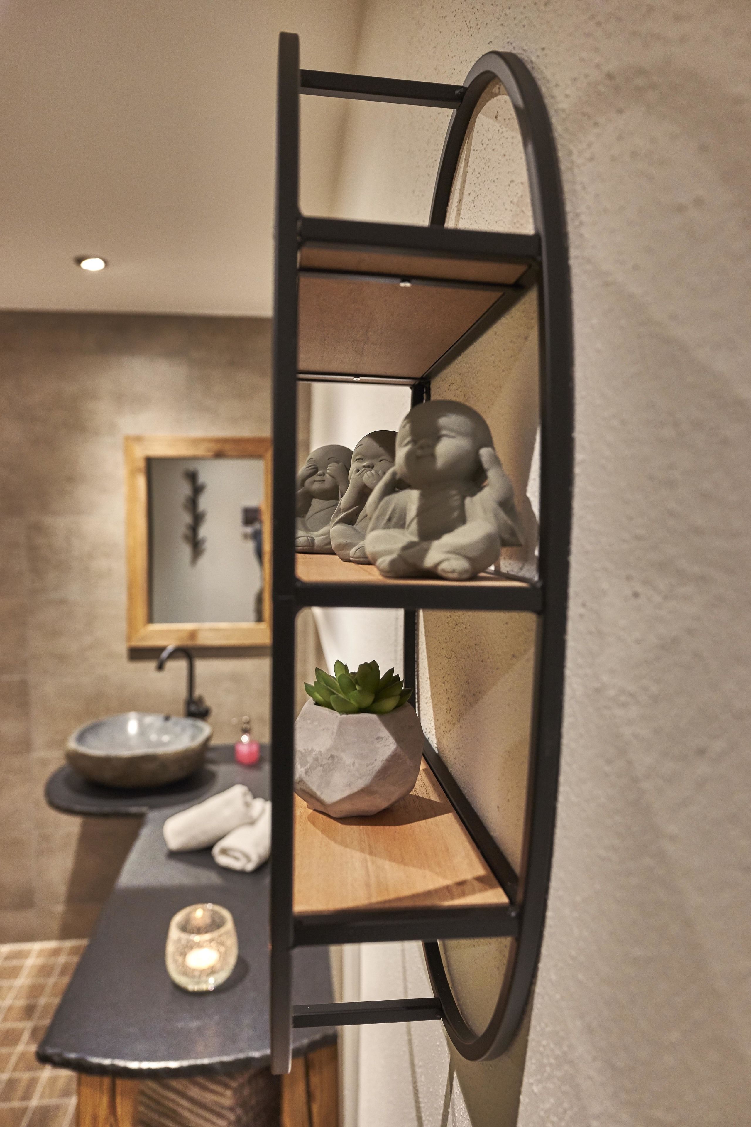 Une salle de bain avec un meuble-lavabo en bois, un évier, un miroir et une étagère ornée d’objets décoratifs.