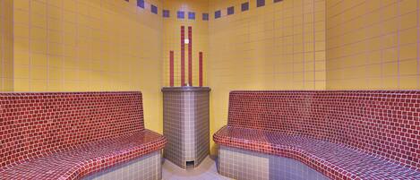 A spa room with two red and gray tiled benches, a central pillar, and yellow tiled walls.