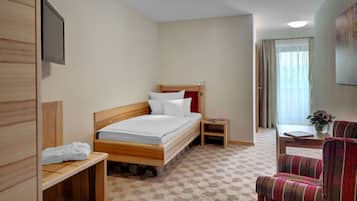 Een hotelkamer met een houten bed, een klein nachtkastje, een stoel, een bureau en een raam met gordijnen.