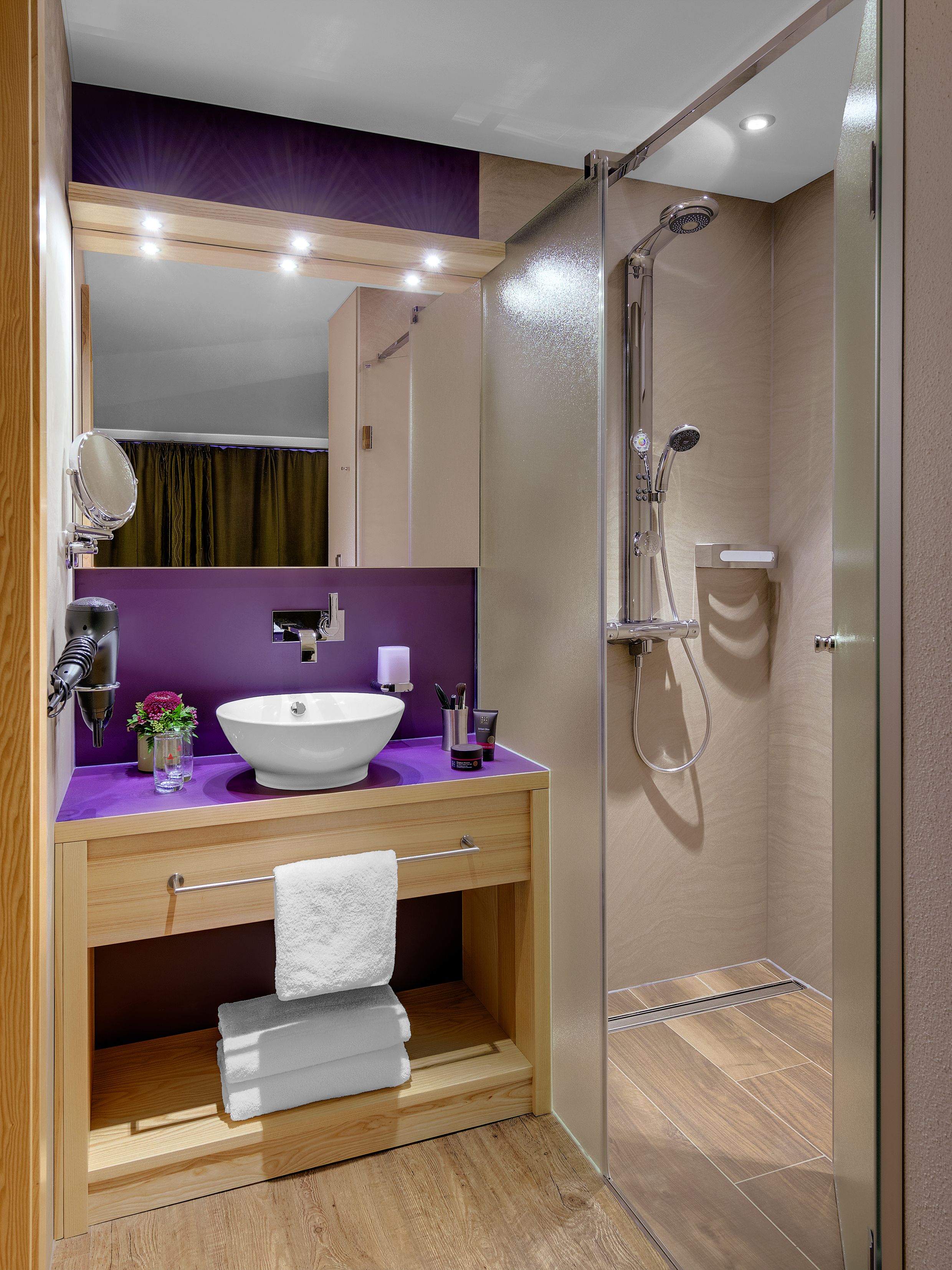 A modern bathroom with a wooden vanity, a large mirror, a white sink, and a glass-enclosed shower.