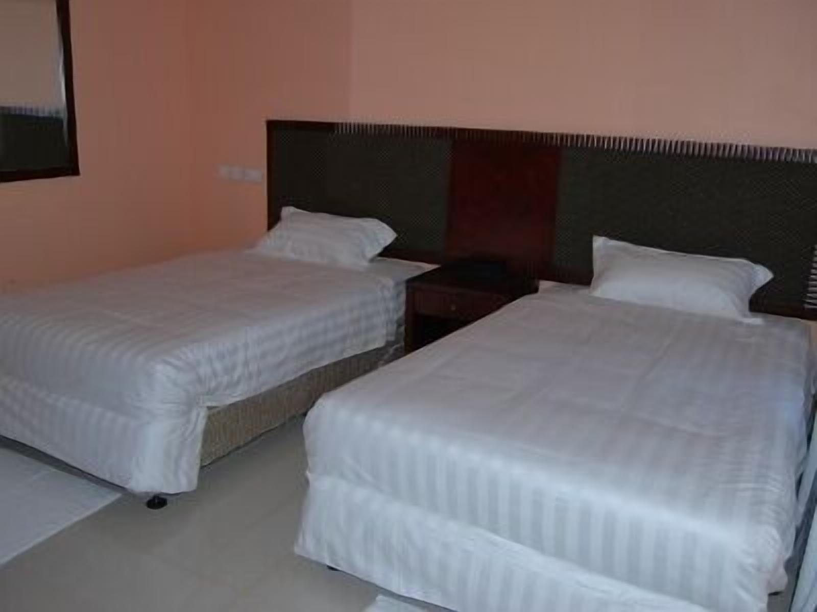 Dos camas individuales con ropa blanca en una habitación con paredes color melocotón y cabecera oscura.