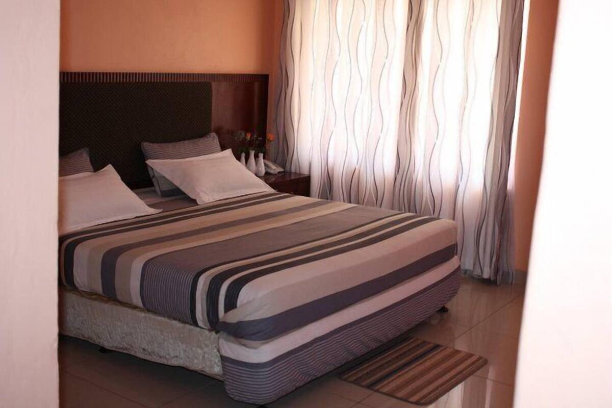 A neatly made double bed with striped bedding, a headboard, and a nightstand with a vase of flowers.