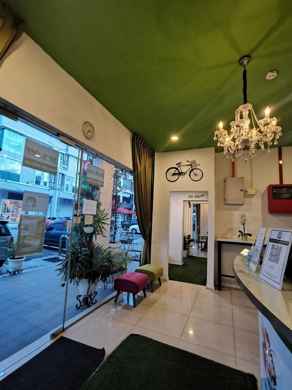 Un hall d’hôtel avec un plafond vert, un lustre, une décoration à thème cycliste et un comptoir d’accueil doté d’un code QR.