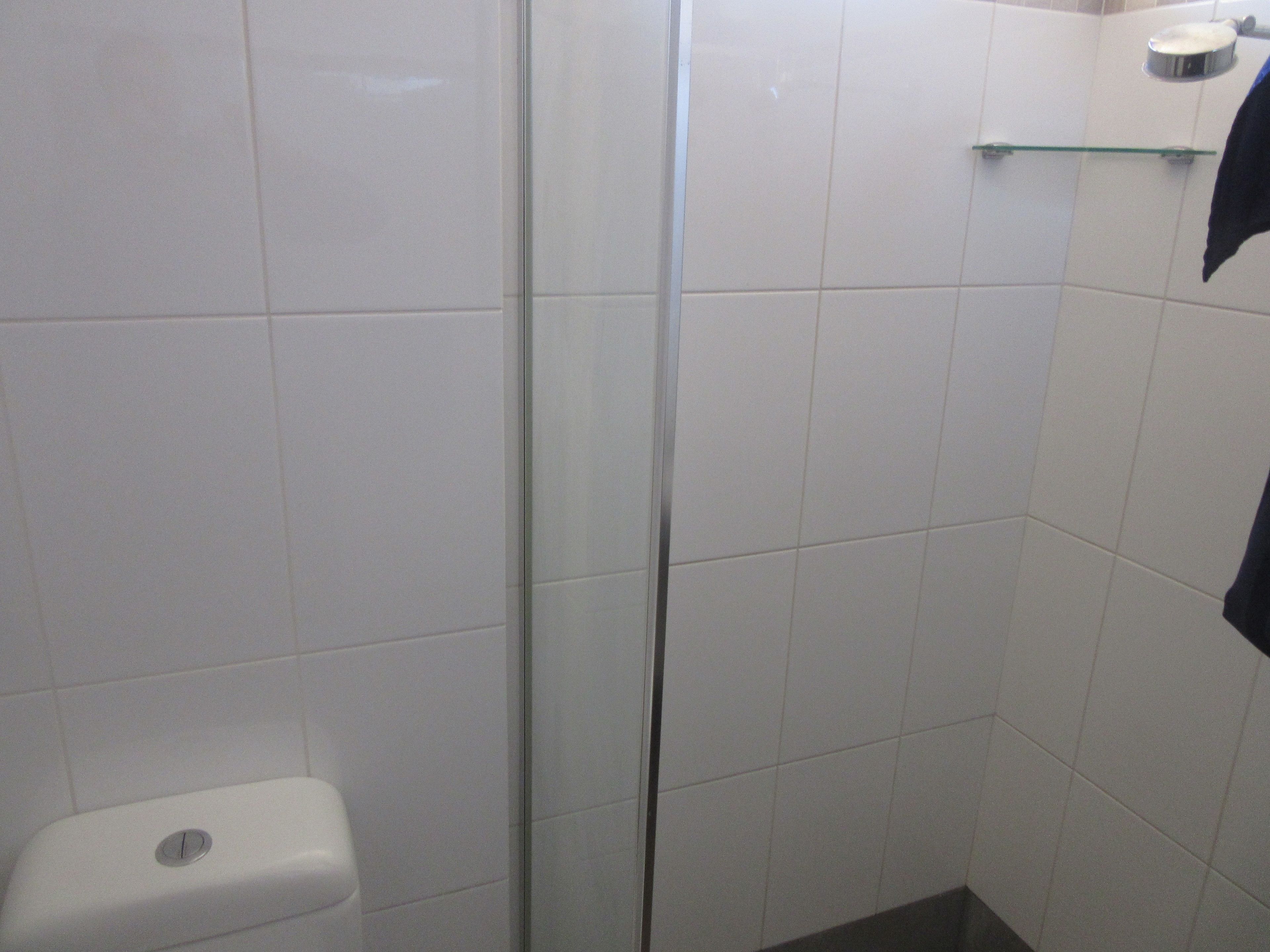 A bathroom with white tiles, a glass shower door, a toilet, and a towel rack.