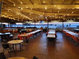 Un área de comedor al aire libre con mesas y sillas, un bar y vistas al mar.