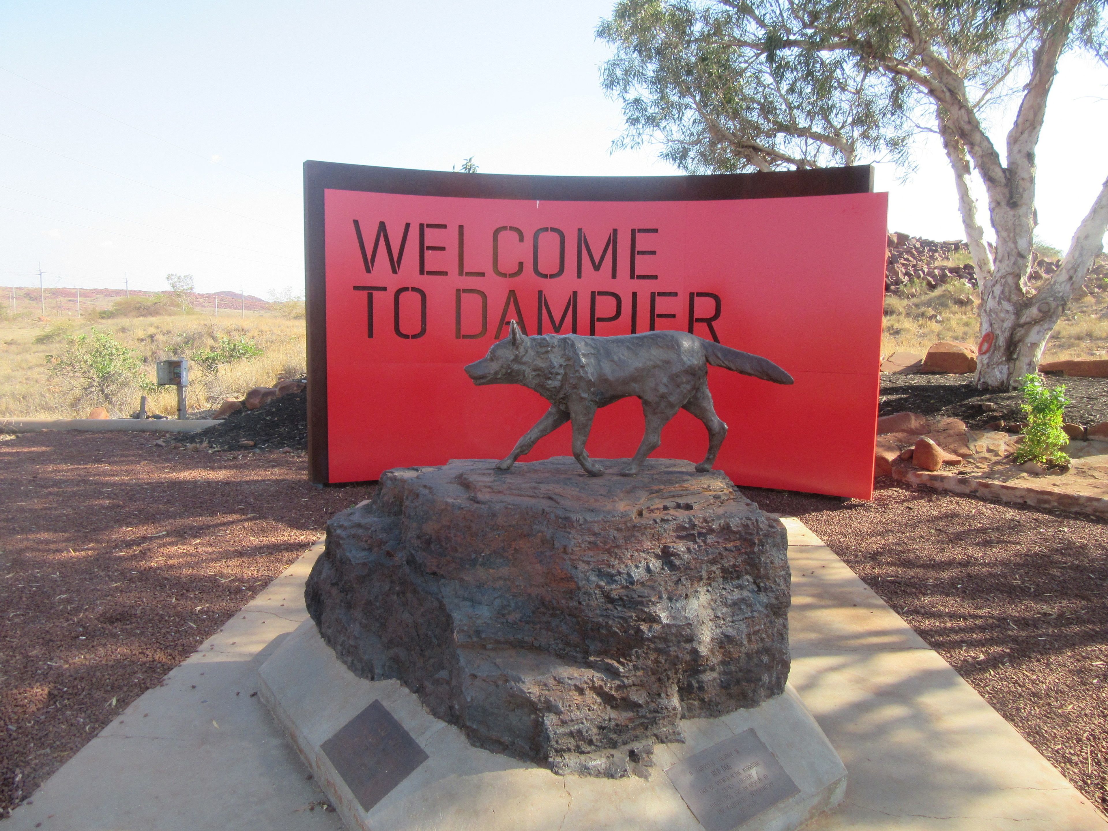 A welcome sign with a wild dog statue in front.