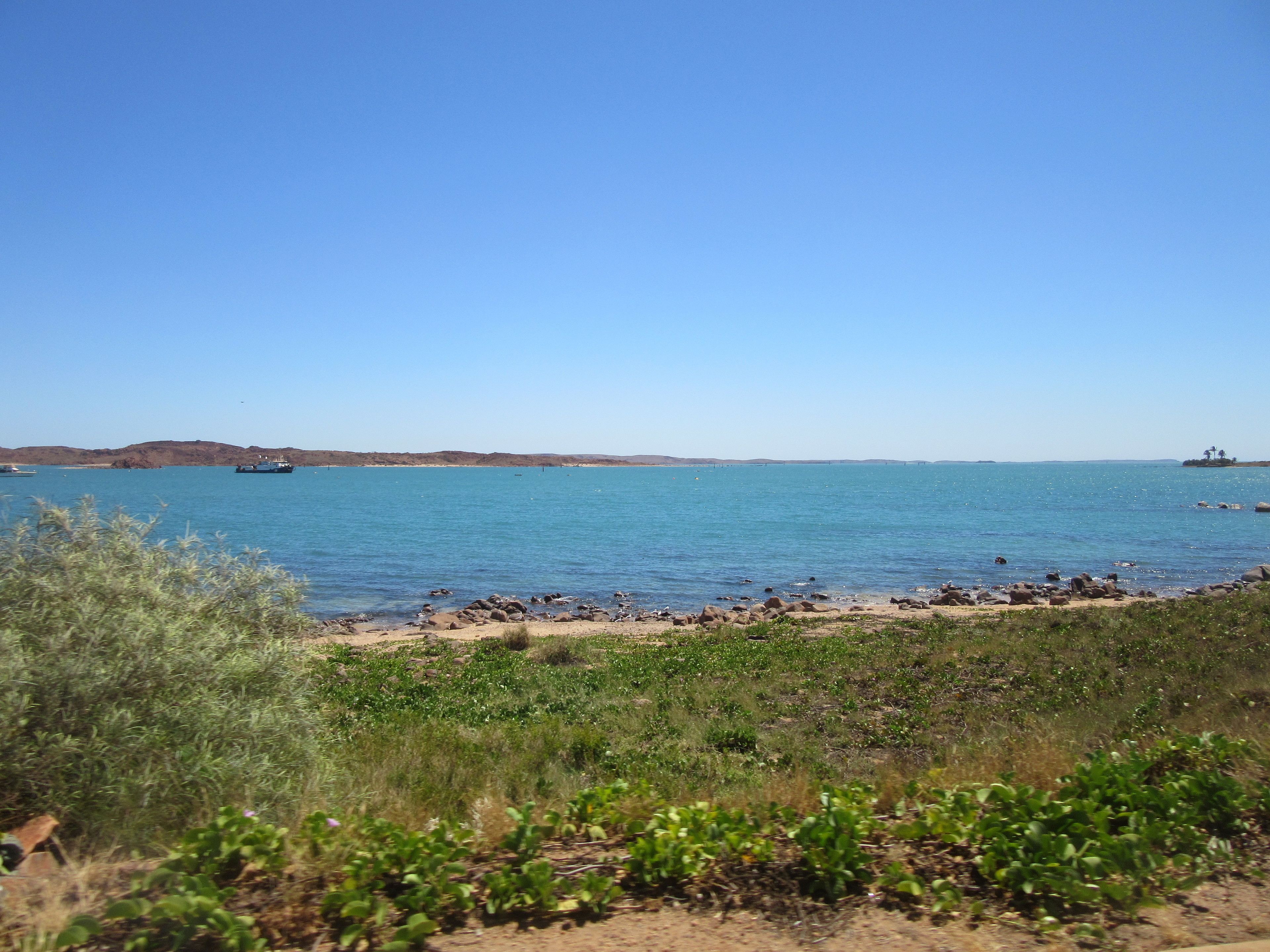 Un paisaje costero con cielo despejado, una playa arenosa y un litoral rocoso.