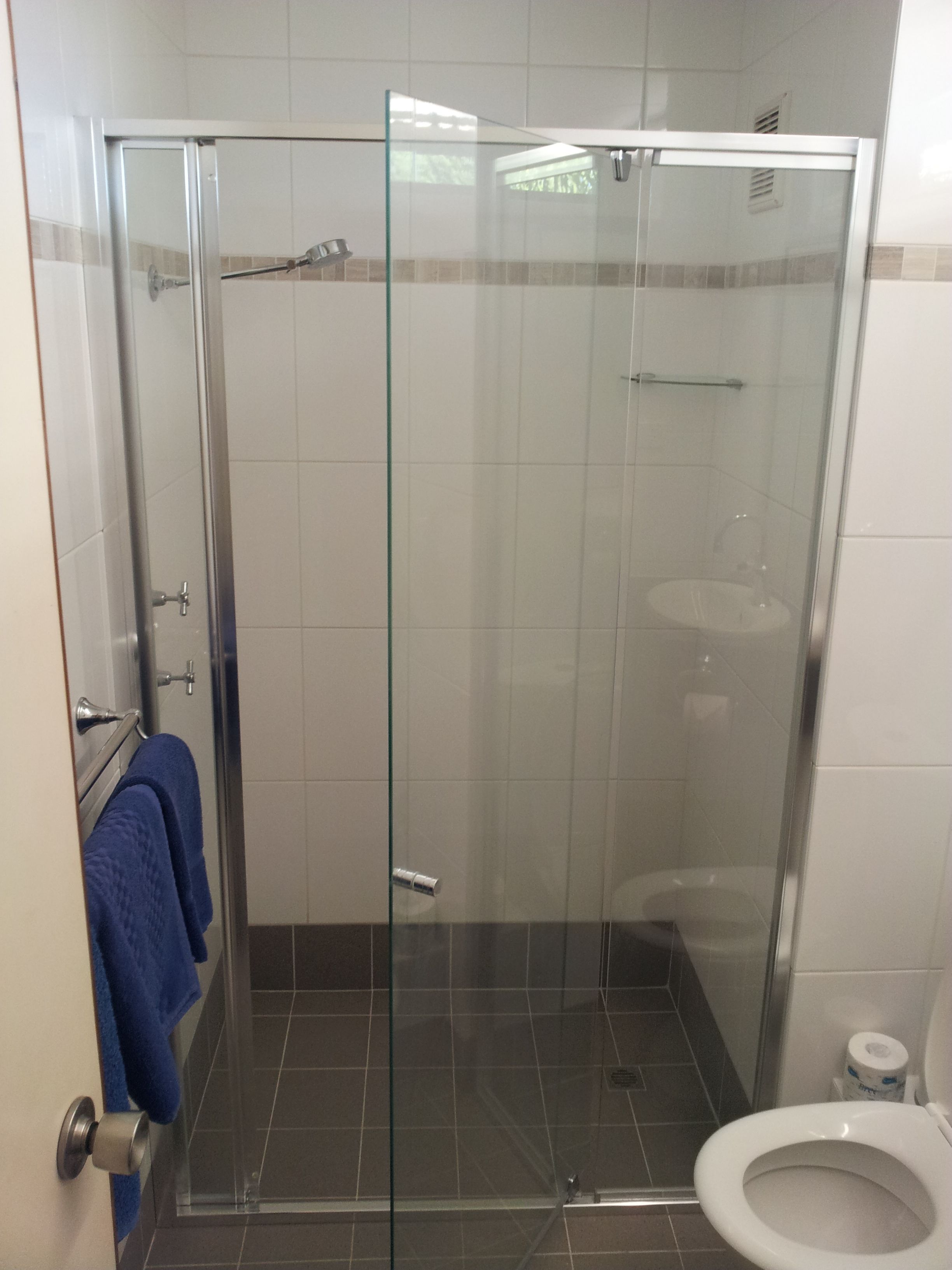 A glass-enclosed shower stall with a white toilet and a blue towel hanging on the door.