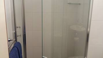A glass-enclosed shower stall with a white toilet and a blue towel hanging on the door.