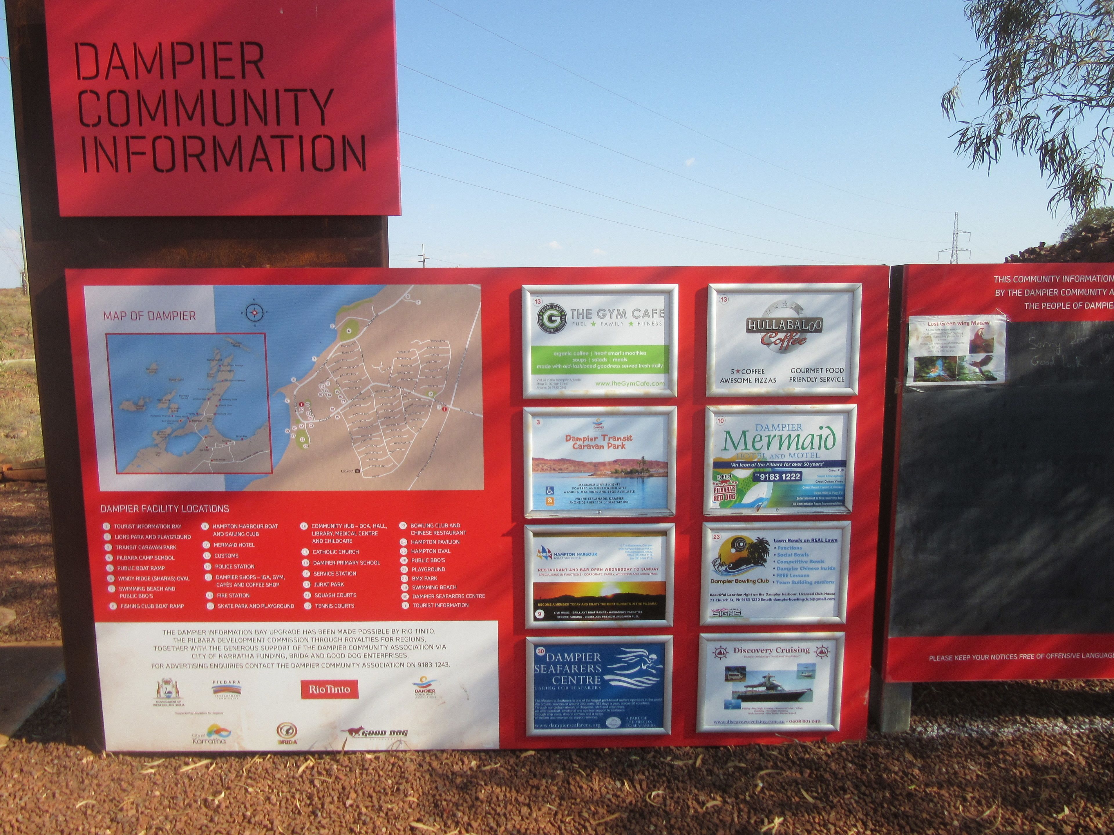 A community information board with a map of Dampier, listing local facilities like a tourist information center, marina, and schools.