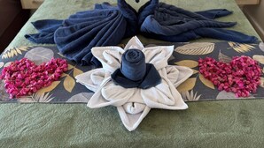 Una cama bien hecha con toallas y flores dispuestas sobre el cubrecolchón.