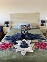 Una cama bien hecha con toallas y flores dispuestas sobre el cubrecolchón.