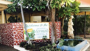 Letrero de bienvenida del Hotel y Motel Mermaid, con un muro de piedra y un pequeño estanque con plantas.