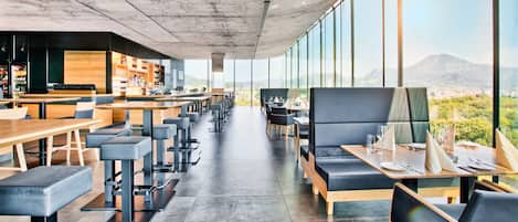 A modern restaurant with a long counter, bar area, and seating with a view of the mountains.