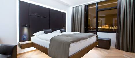 Un dormitorio moderno con una cama grande, una mesita de noche y vistas a la ciudad de noche.