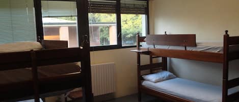 A dormitory room with bunk beds, a radiator, and a window with blinds.