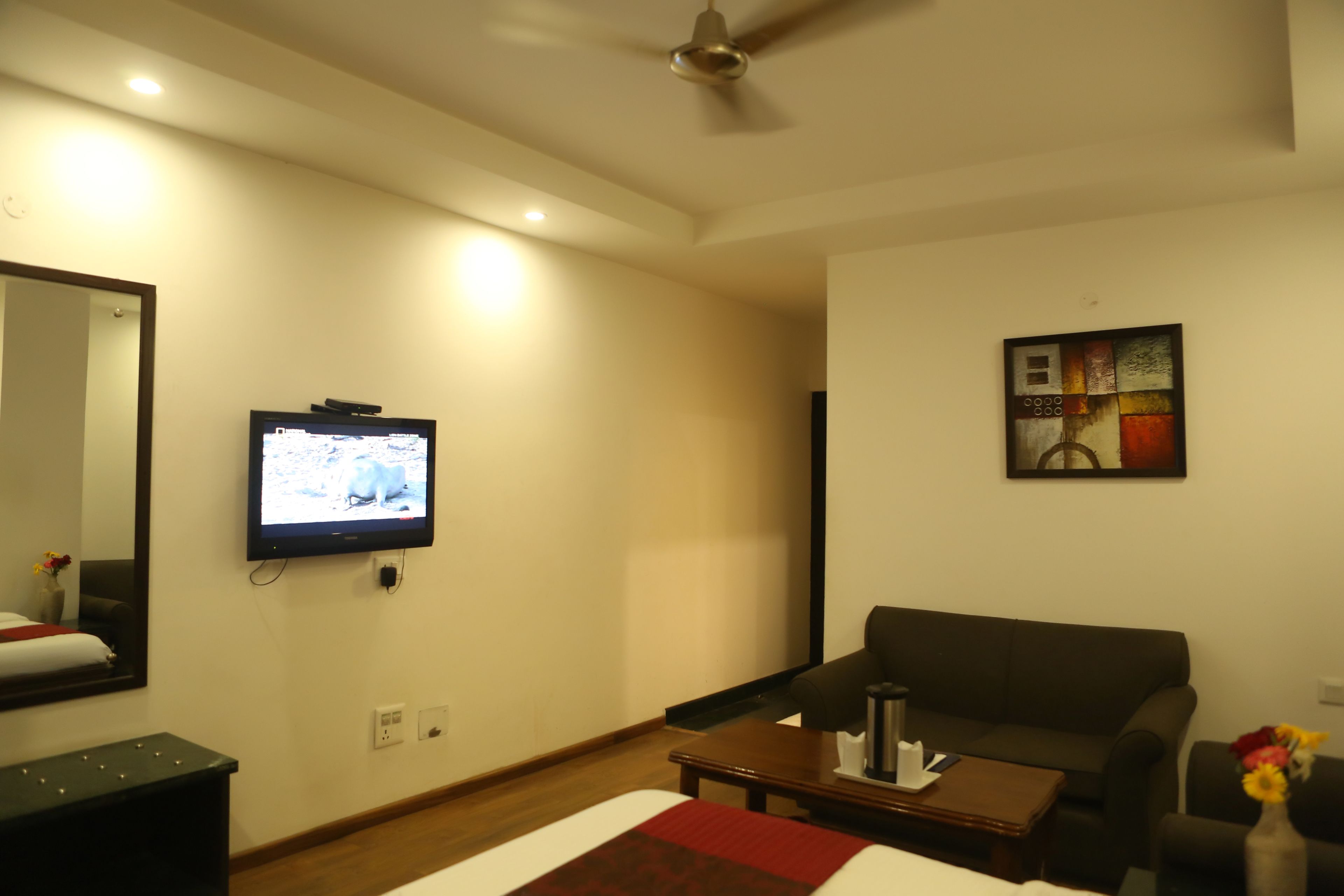A hotel room with a bed, a TV mounted on the wall, a sofa, a coffee table, and a painting on the wall.